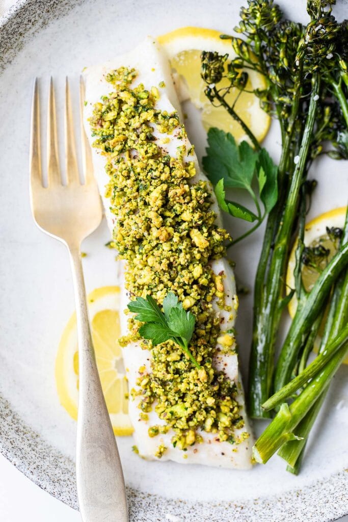A close up look at a piece of baked halibut with a green pistachio crust.