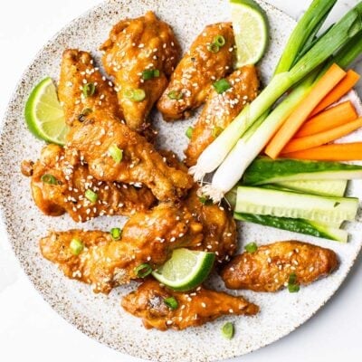 A plate piled with chicken wings drenched in a Thai style hot sauce, with fresh cut carrots and cucumbers.