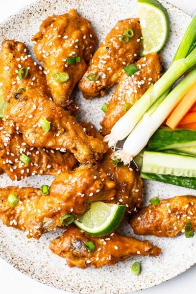 A plate piled with chicken wings drenched in a Thai style hot sauce, with fresh cut carrots and cucumbers.