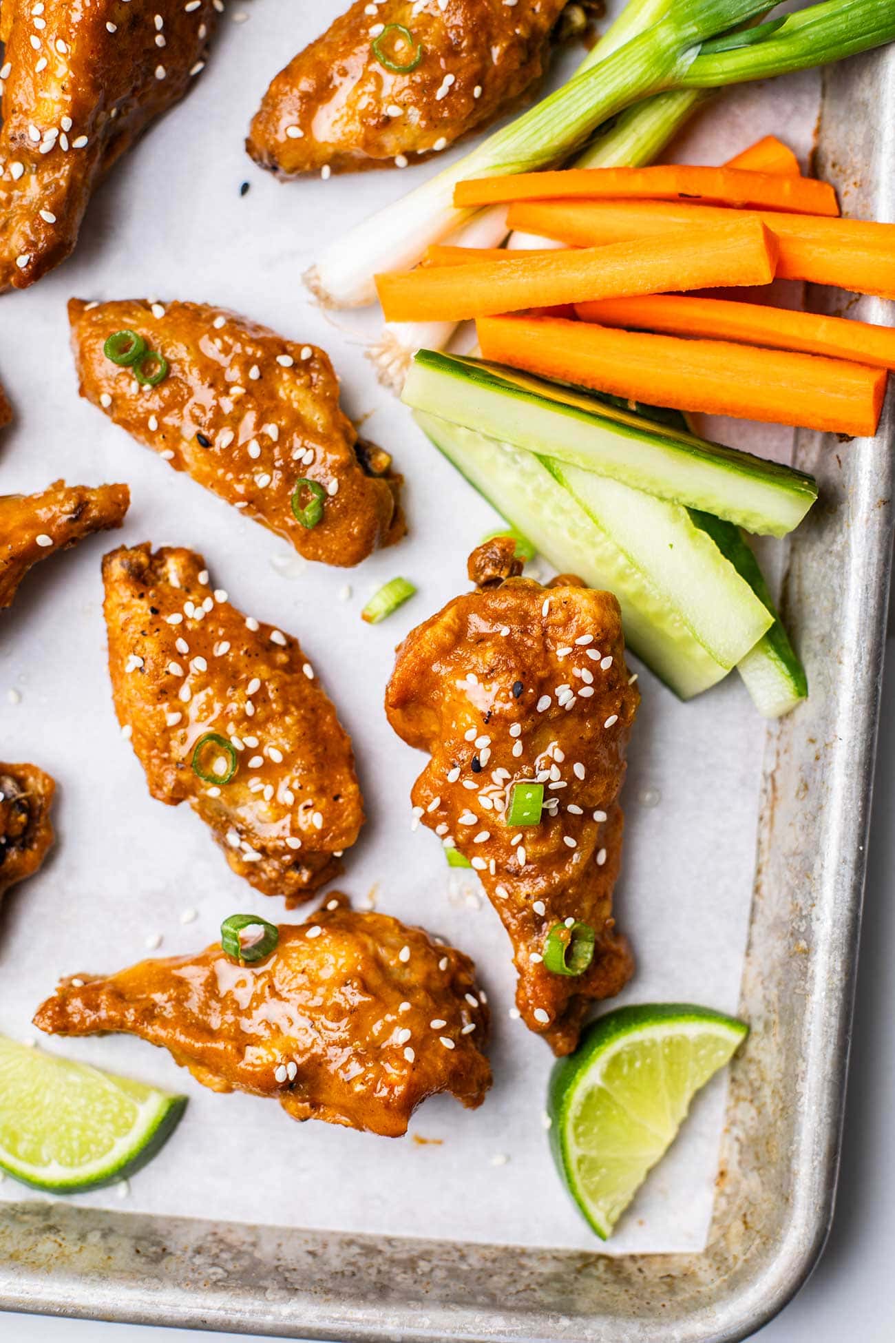 A close up look at crispy chicken wings drenched in a spicy Thai chili sauce and served with cucumbers and carrots.