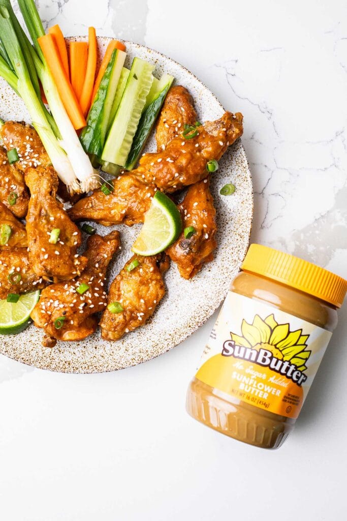 A plate of Thai chicken wings next to a jar of SunButter.