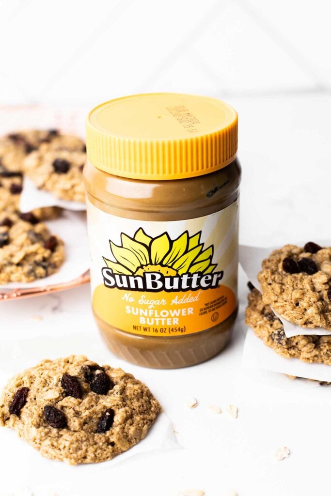 A jar of SunButter sitting next to a cooling rack of healthy oatmeal raisin cookies.