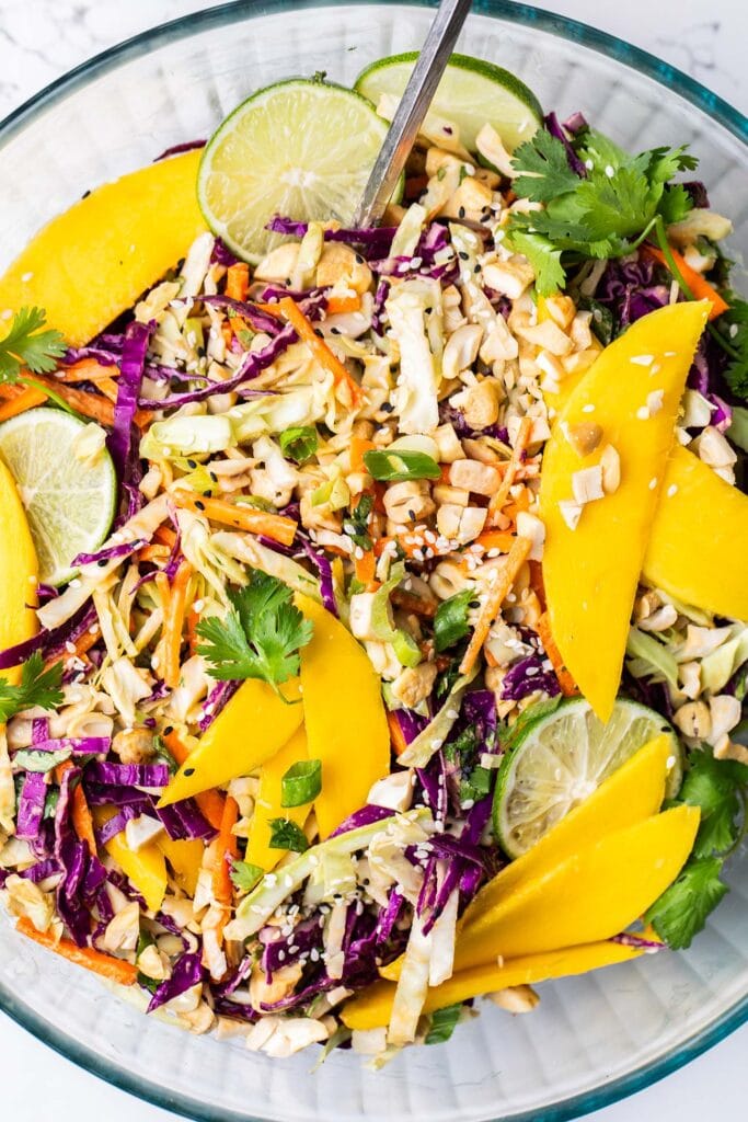 A close up look at the carrot and cabbage salad topped with mango slices and chopped toasted cashews.