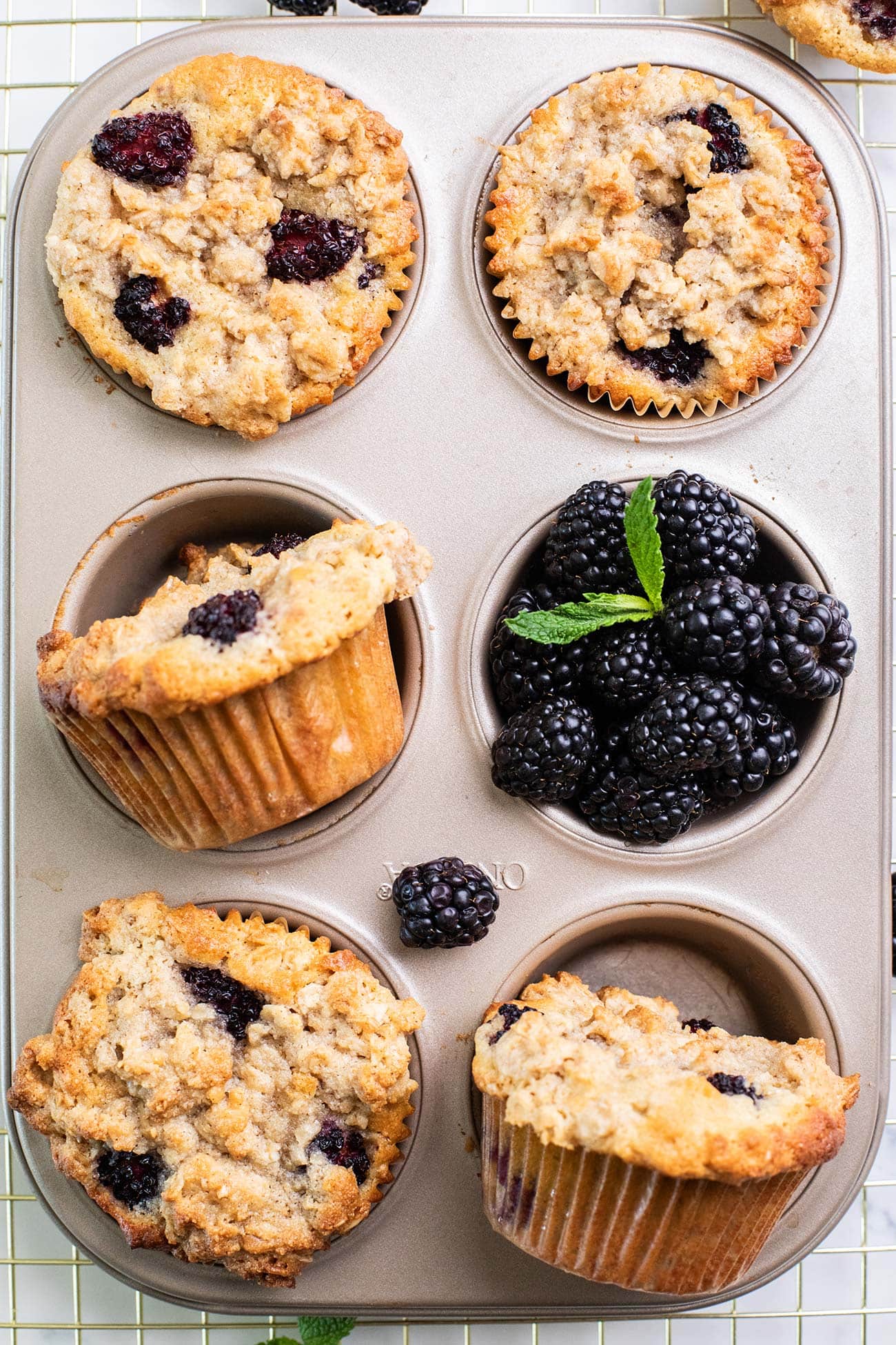 A muffin tin showing healthy blackberry muffins with a golden brown oat topping.