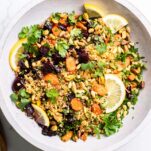 A colorful quinoa salad shown served in a white bowl with a wooden spoon.