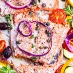 A piece of salmon surrounded by colorful mediterranean style vegetables.