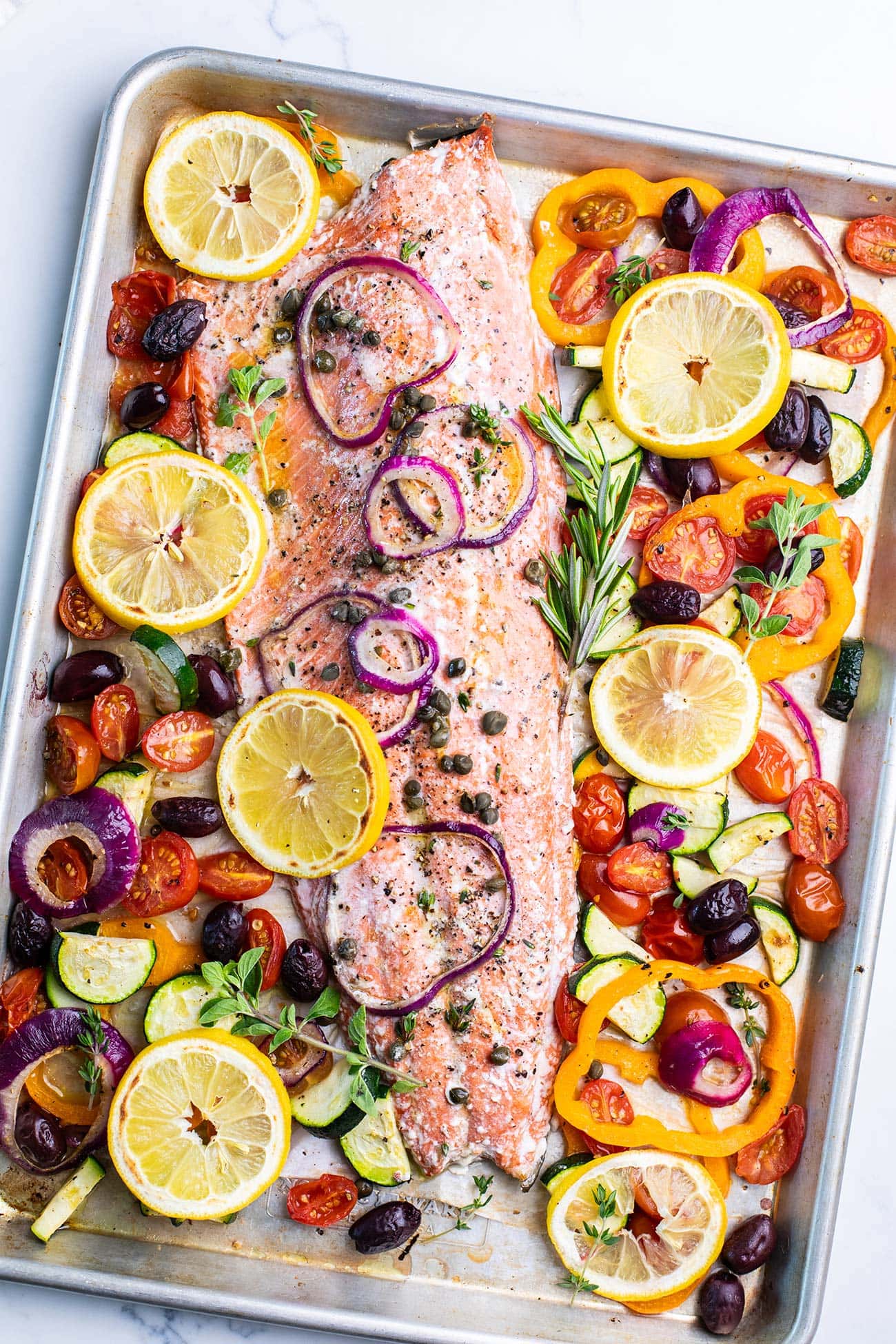 A sheet pan with a salmon filet surrounded by mediterranean vegetables.
