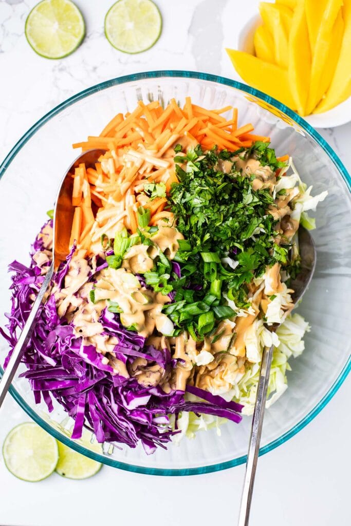 A clear glass salad bowl shown with a cabbage and carrot salad drizzled with a creamy sesame dressing.