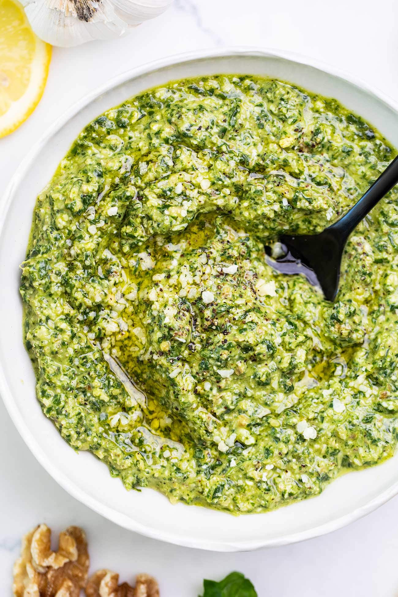 A close up look at a bowl of basil walnut pesto with a black spoon in the center.