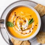 A bowl of creamy tomato soup garnished with basil and served with crackers.