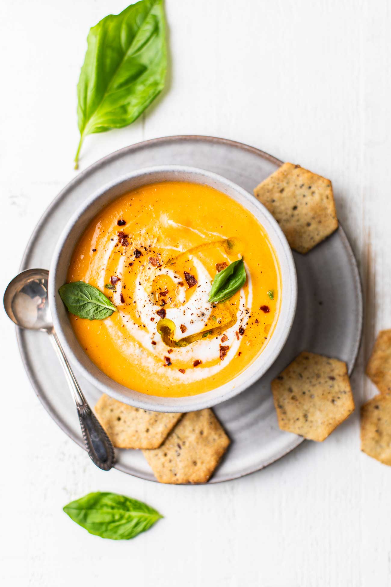 A bowl of tomato soup shown garnished with fresh basil and served with crackers.