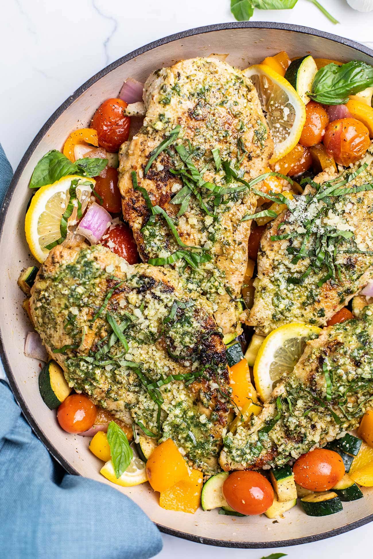 A skillet shown with lots of colorful veggies sauteed with pesto coated chicken.