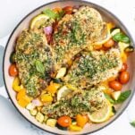 4 chicken breasts coated with pesto sitting in a skillet with colorful vegetables.