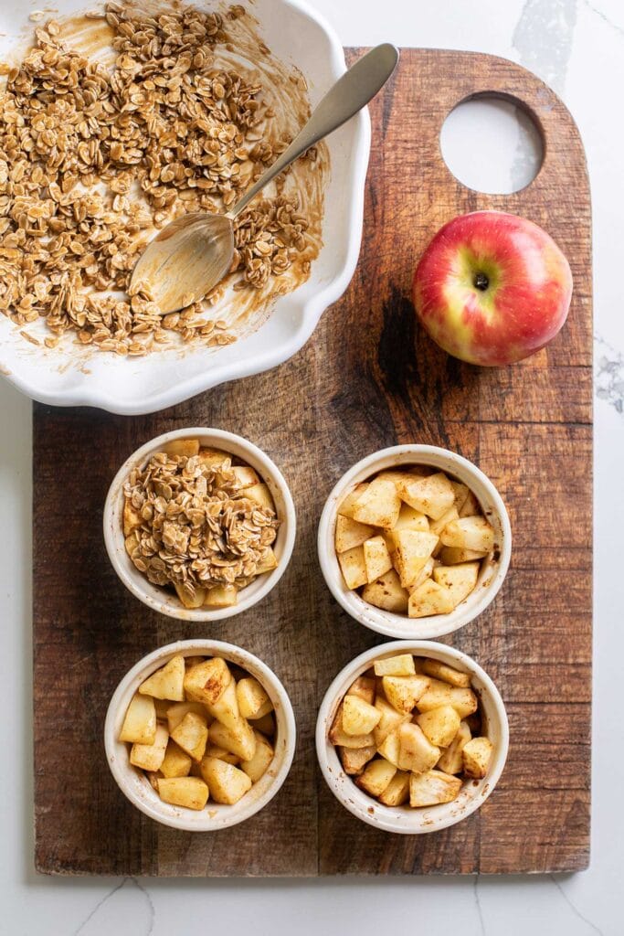 The ramekins with cooked apples being topped with the crisp topping.