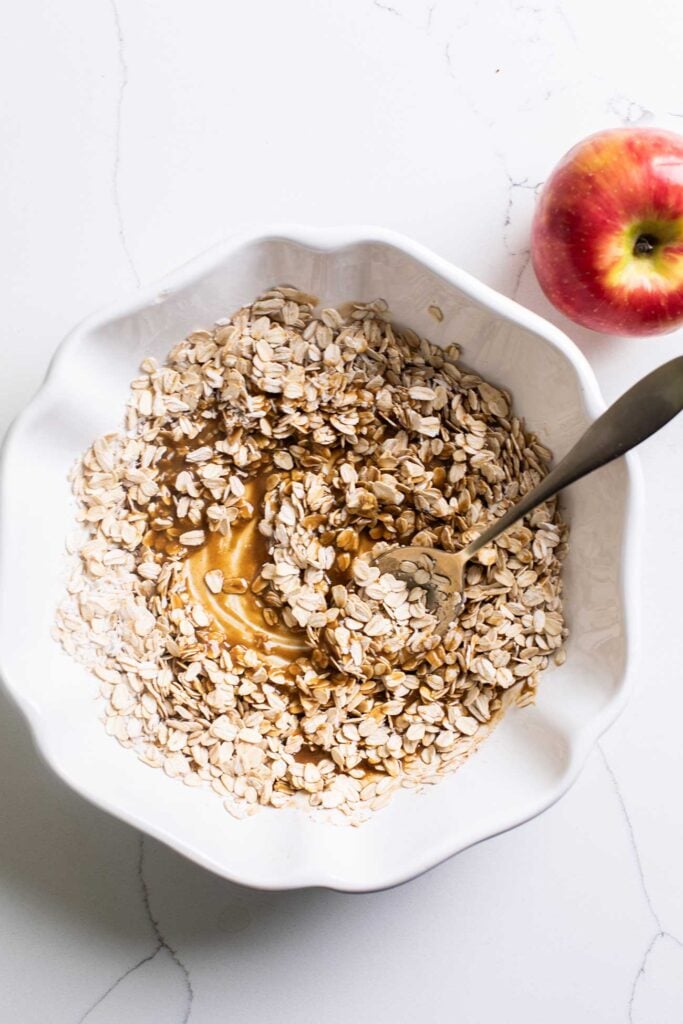 A bowl showing the oats and coconut being added to the crisp topping mixture.