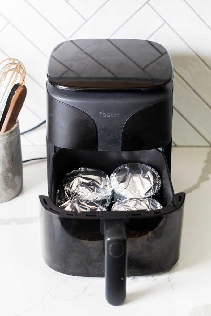 Ramekins covered in foil going in to an air fryer.