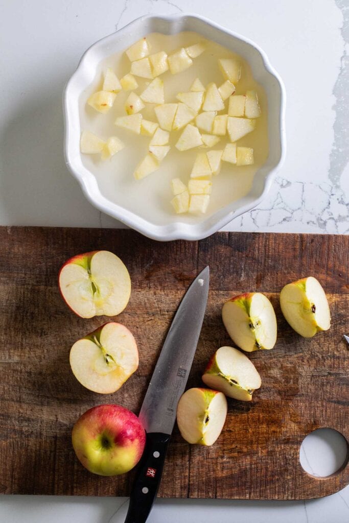 A cutting board with apples being peeled and diced.