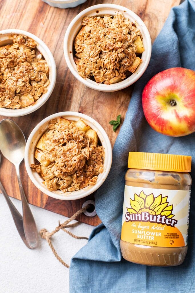 Ramekins with apple crisp sitting next to a jar of SunButter sunflower seed butter.