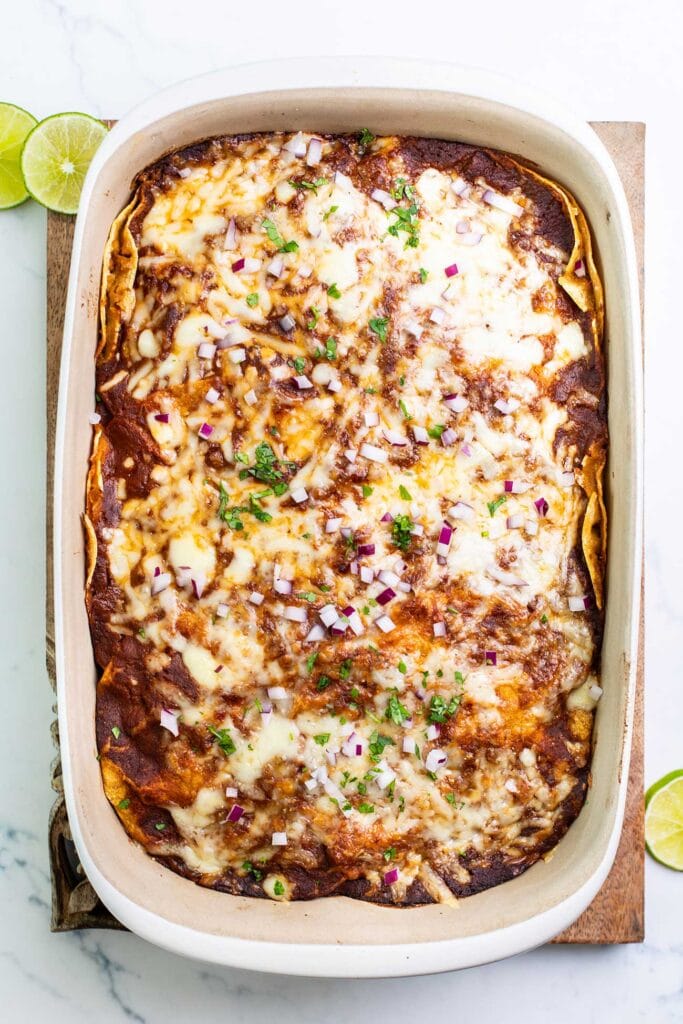 An enchilada casserole shown garnished with onions and cilantro.