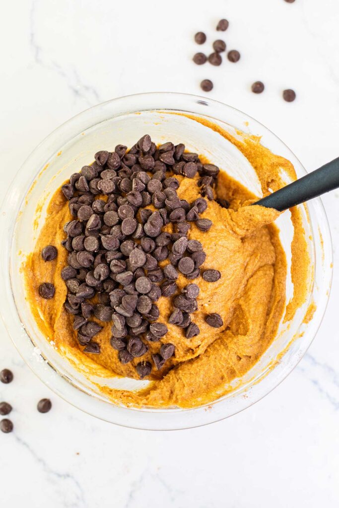 Chocolate chips being folded into an orange pumpkin muffin batter.