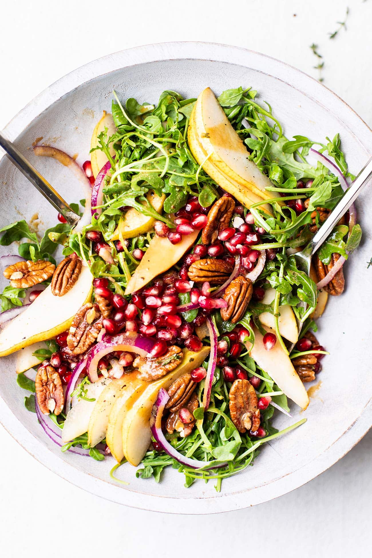 A white salad bowl filled with a pear and rocket salad tossed with a creamy balsamic dressing.