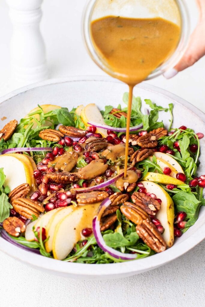 A creamy balsamic dressing being drizzled over a pear and rocket salad.