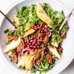 A pear and rocket salad shown being tossed with a creamy balsamic dressing.