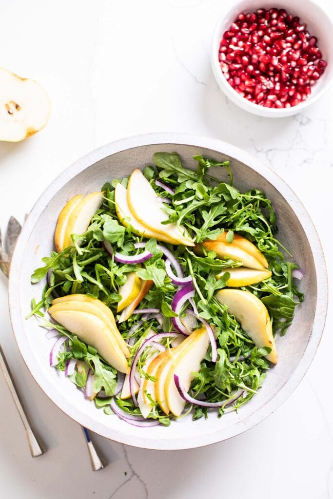 A bowl of arugula with pears and onions.