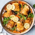 A cast iron dish shown with chicken thighs baked with lemon slices.