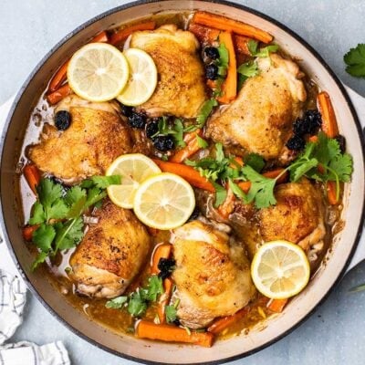 A cast iron dish shown with chicken thighs baked with lemon slices.