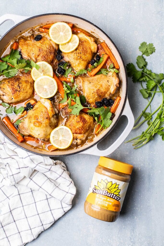 A pan of baked moroccan chicken shown with a jar of sunbutter.