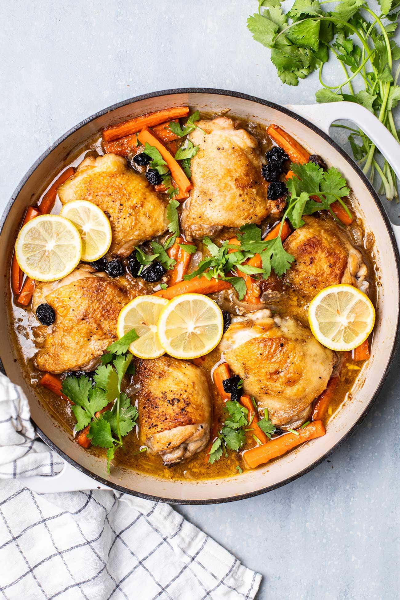 A large cast iron pot with chicken tagine garnished with cilantro and lemons.