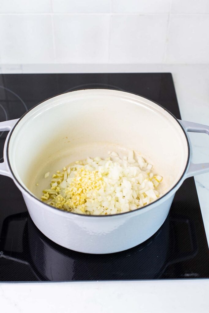 A dutch oven shown with garlic and onions being sauteed.