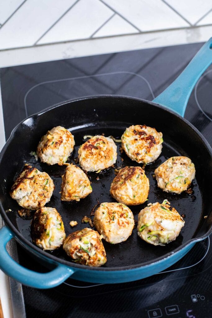 Meatballs shown being browned in a skillet.