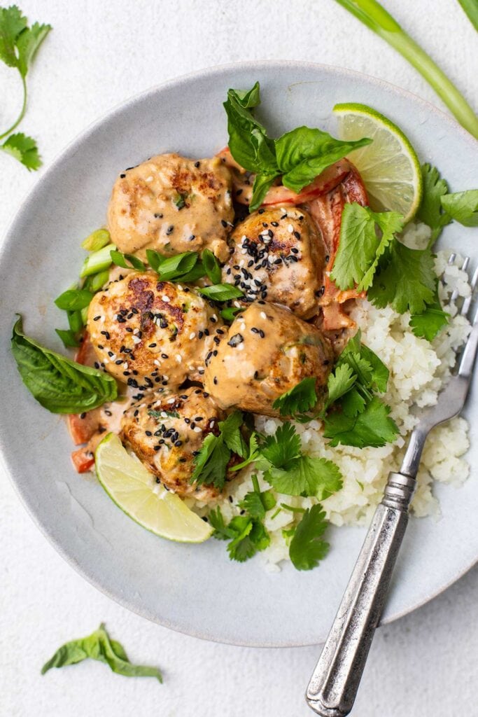 Showing how to serve Thai chicken meatballs over cauliflower rice garnished with herbs.