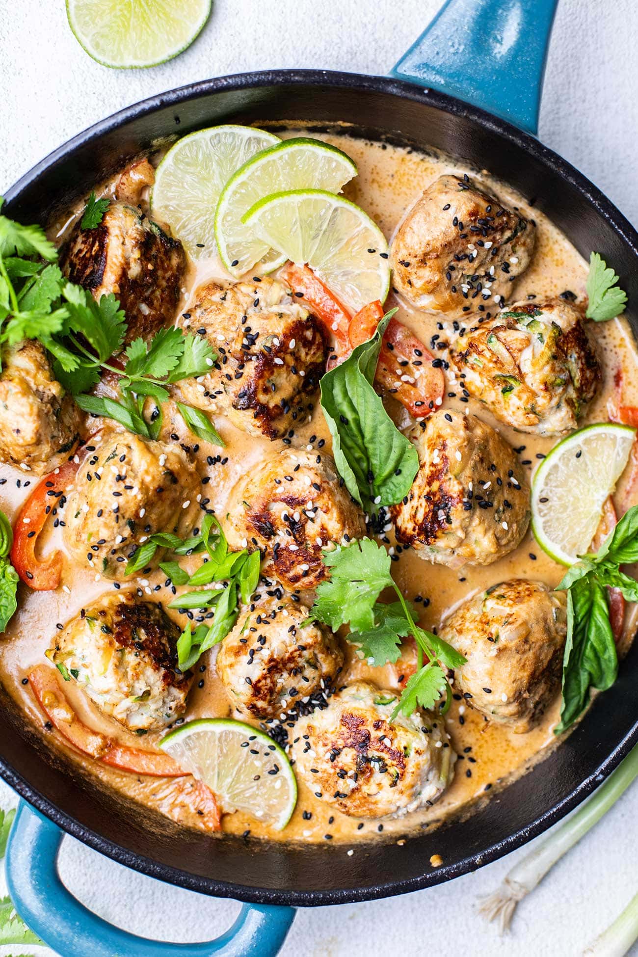 A skillet filled with thai chicken meatballs in a creamy coconut sauce.