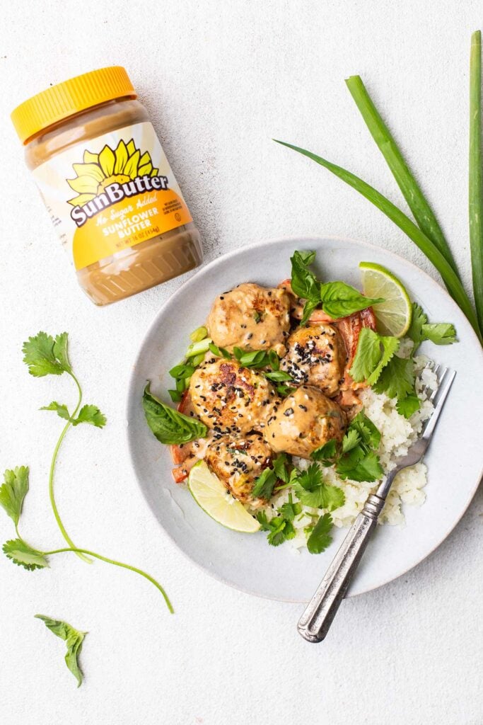 A jar of SunButter next to a plate of Thai chicken meatballs served over cauliflower rice.