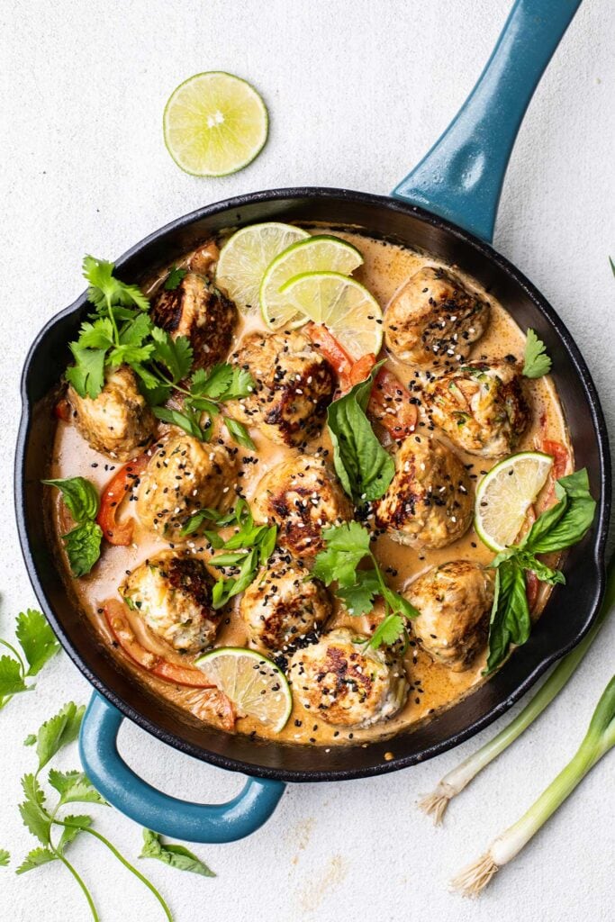 Meatballs added back into the skillet with the coconut sauce, garnished with fresh herbs and lime.