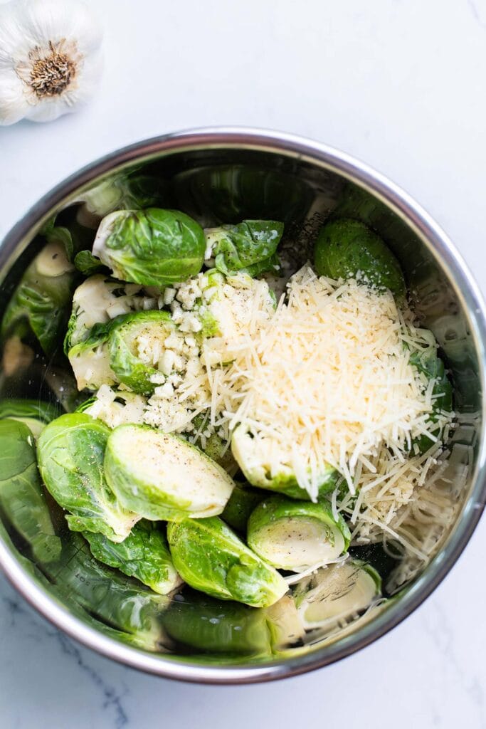 Brussels sprouts in a large bowl being combined with parmesan cheese, garlic, lemon juice, and avocado oil.