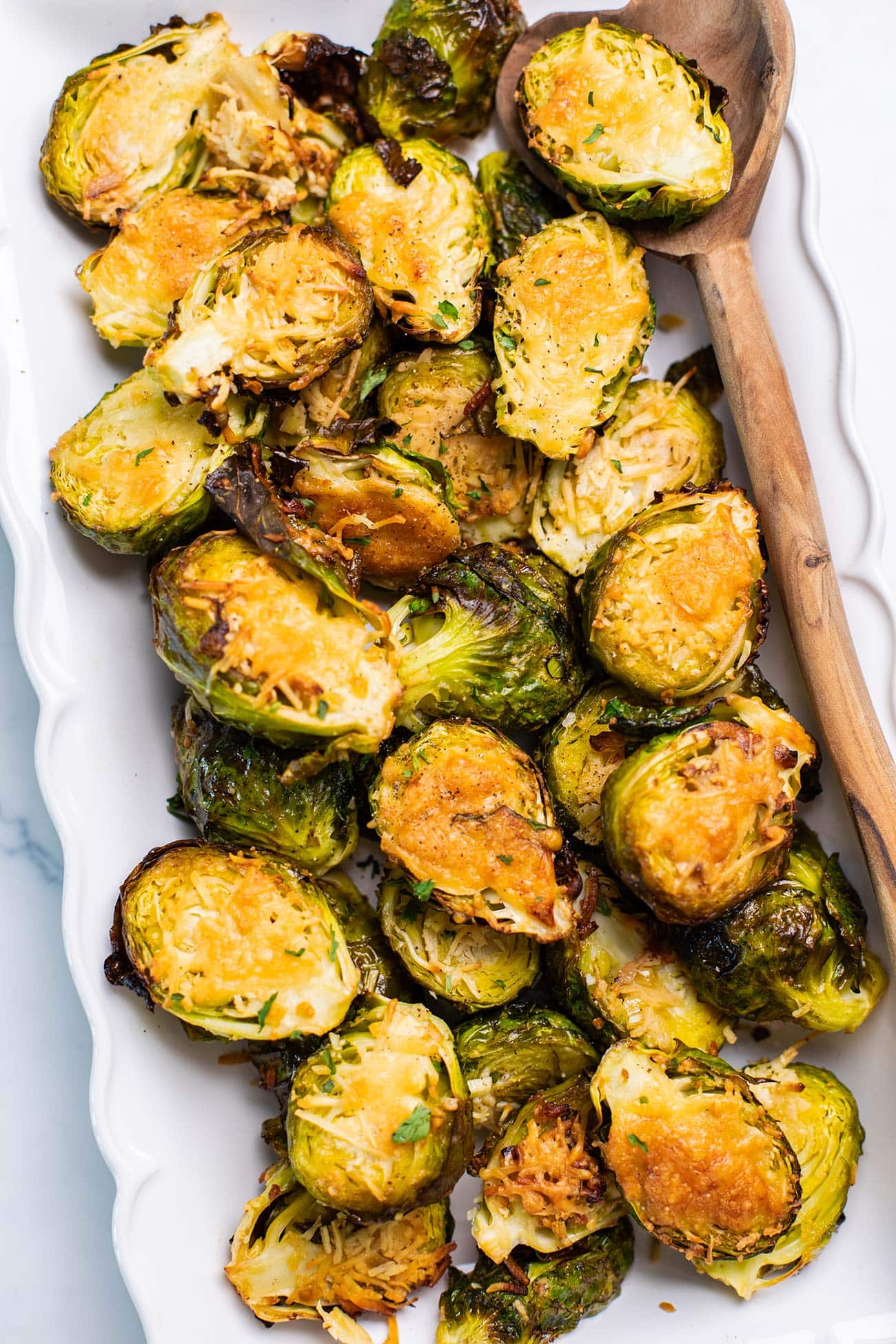 A white serving platter with brussels sprouts with a crispy parmesan crust.