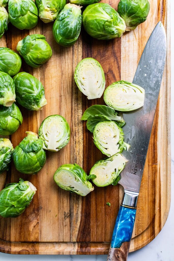 A cutting board showing Brussels sprouts being cut in half.