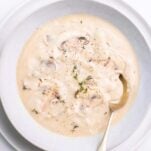 A bowl of cream of mushroom soup garnished with thyme.