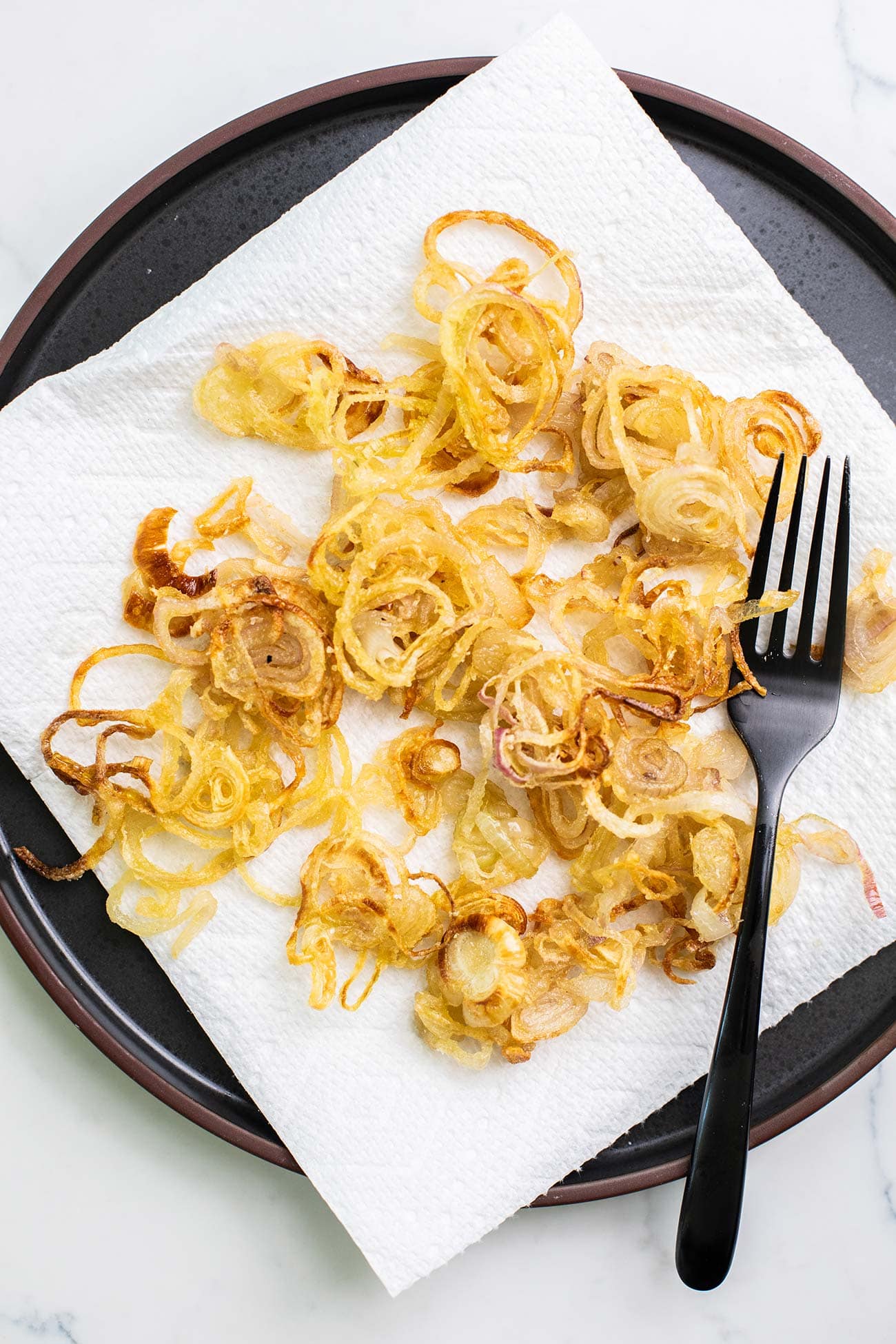 Crispy browned shallots cooling on a paper towel lined plate.