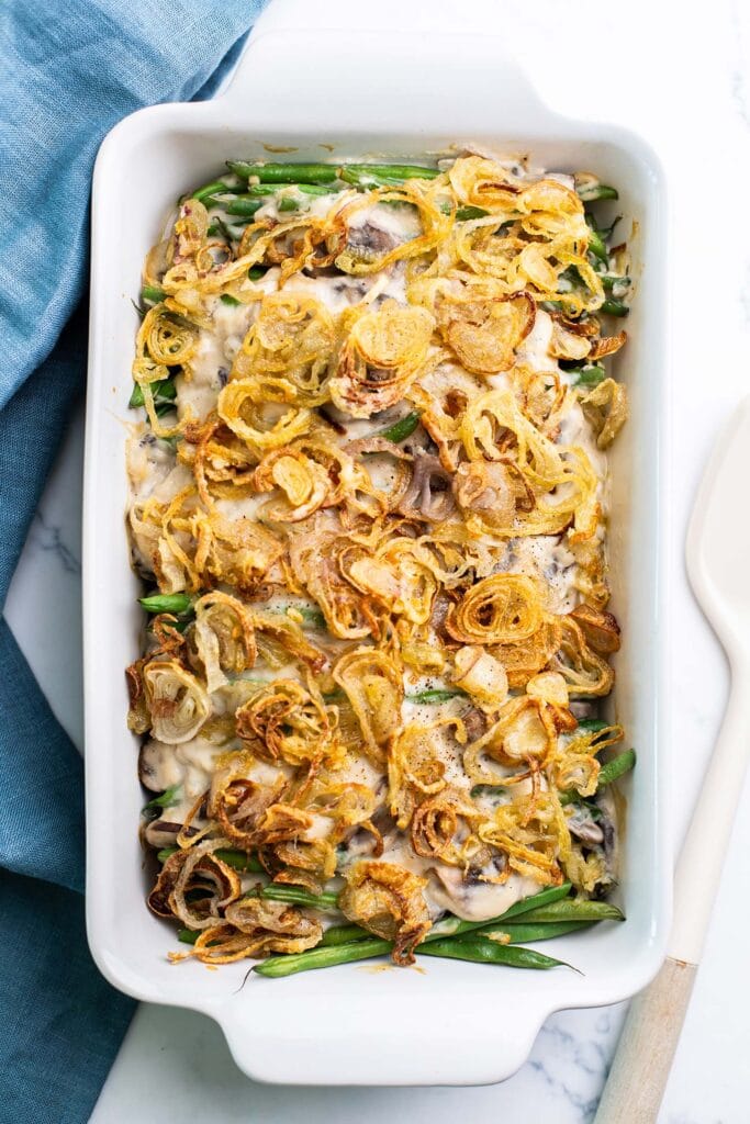 A white casserole dish with a green bean casserole topped generously with crispy fried shallots.