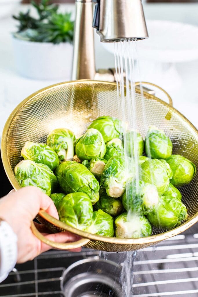 A gold colander showing brussels sprouts being washed.