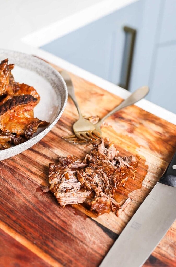 Showing the ribs being shredded with two forks on a cutting board.