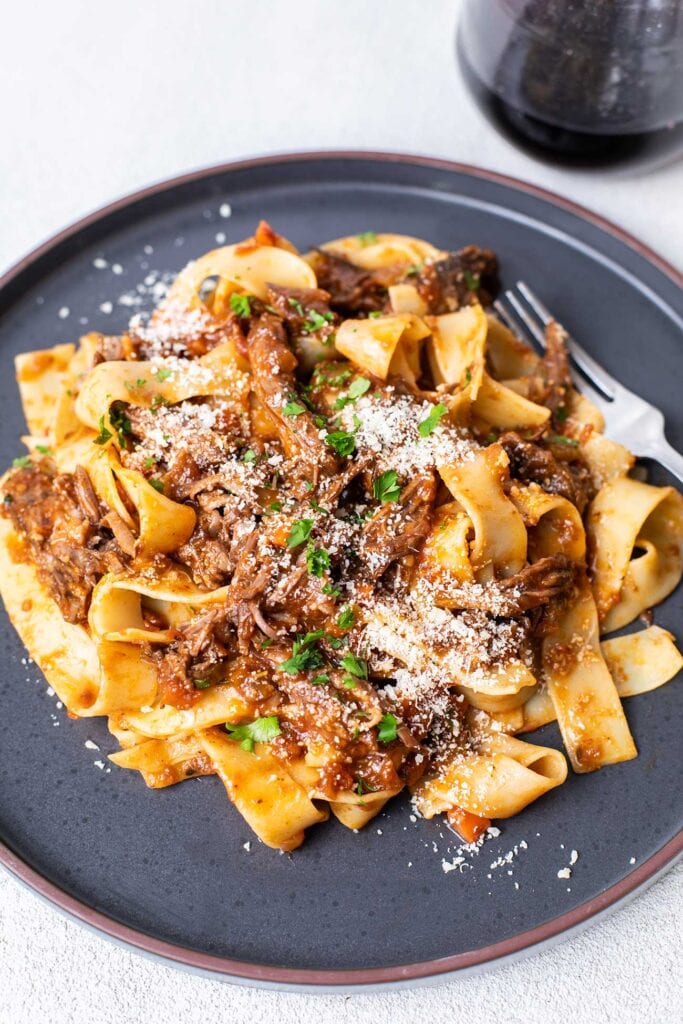 The short rib ragu tossed with pasta, shown garnished with parsley and parmesan cheese.