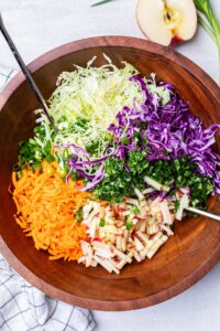 A close up look at the colorful cabbage, carrots, and herbs in a large wooden salad bowl.