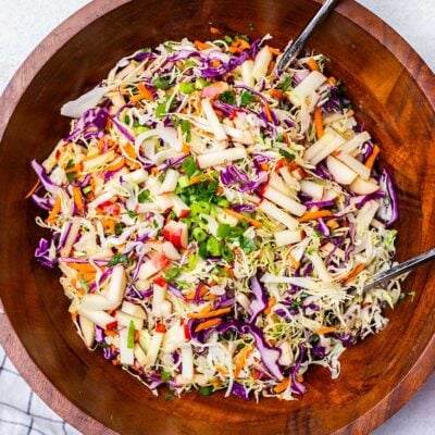 A close up look at a crunchy apple slaw in a large wooden bowl.