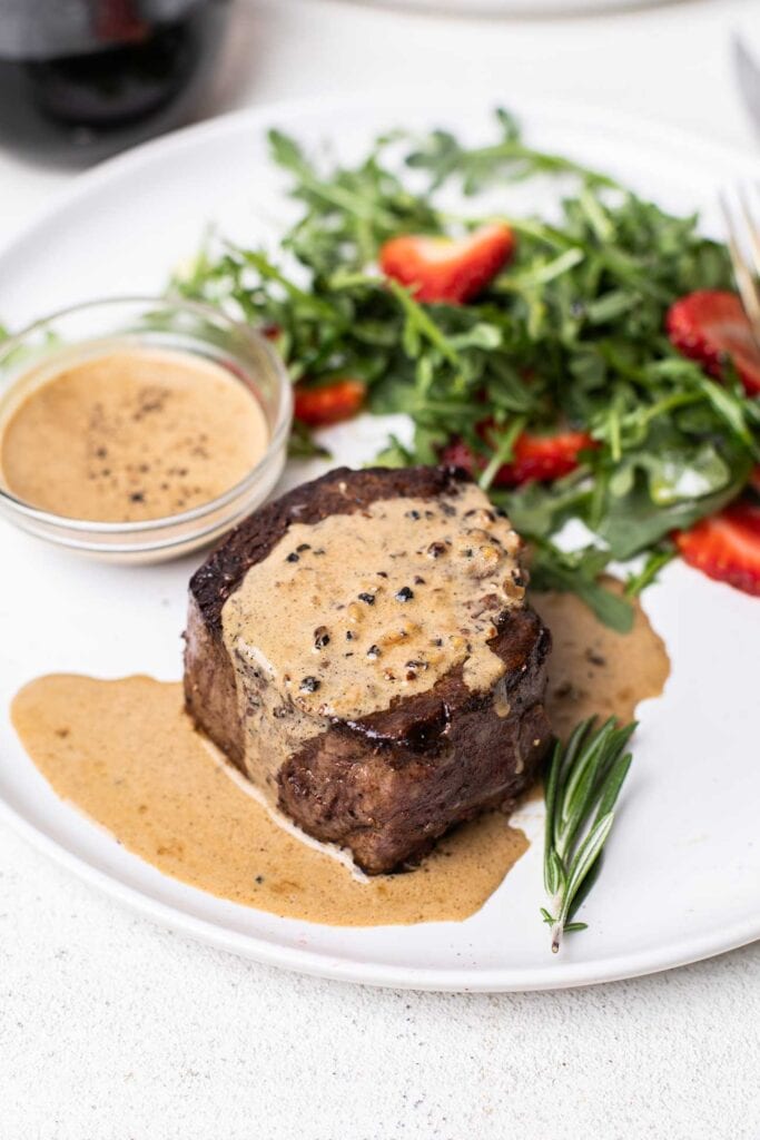 A filet mignon steak shown drizzled with a creamy peppercorn sauce.